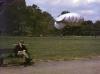 Um homem sentado num banco de jardim, em Londres, lendo um livro. Também um "balão barragem" é visível no fundo, enquanto um segundo voa alto a alguma distância.