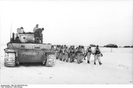 Tanque Tiger I a acompanhar coluna de infantaria em marcha com camuflagem branca numa estrada com neve.