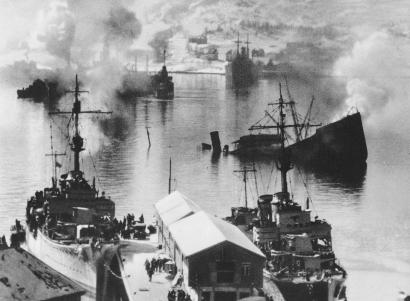 Navios de guerra a arder num porto depois de um ataque aéreo.